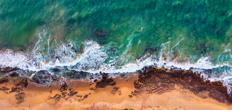 Aerial view of waves breaking on rocks and sand at Rushikonda beach, Visakhapatnam